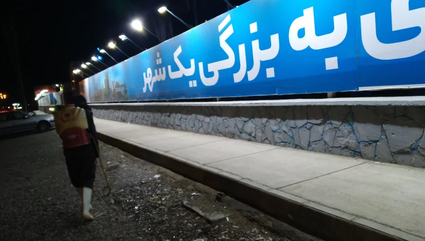 کارگر مجهز به سم‌پاش پشتی در حال اجرای عملیات ضدعفونی و سم‌پاشی در محوطه ایستگاه راه‌آهن در شب، جهت کنترل آفات و بهبود بهداشت محیط.