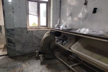 کارگر در حال بررسی و پاک‌سازی فضای آشپزخانه صنعتی با دیوارهای کاشی‌کاری شده، به عنوان بخشی از فرآیند آماده‌سازی برای سم‌پاشی و ضدعفونی محیط.